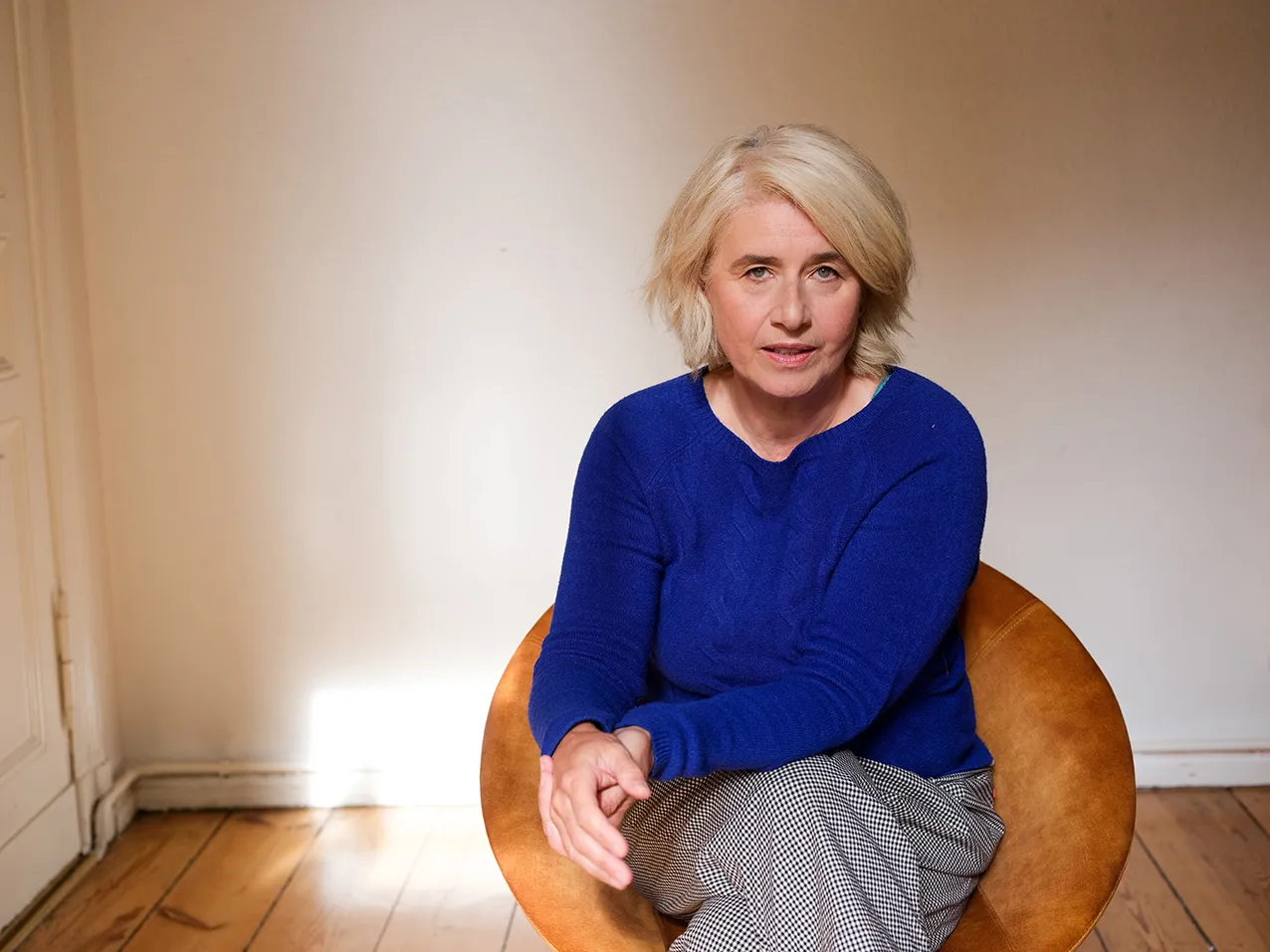 Angelika Fink im blauen Pullover, sitzend in einem hellen Raum mit Holzboden