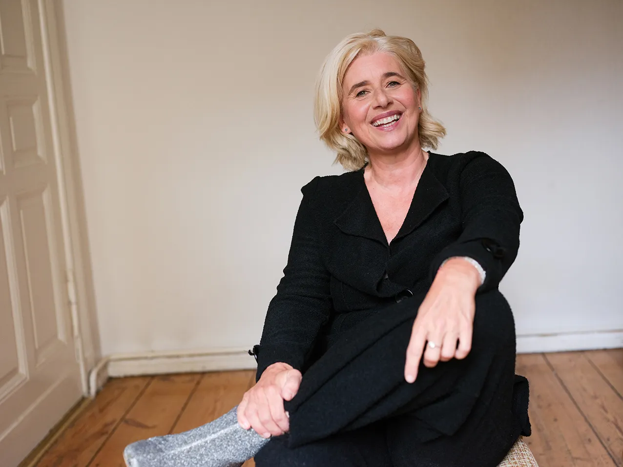 Angelika Fink in schwarzem Kleid, am Boden eines hellen Raums sitzend
